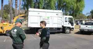 photo of two professional tree trimmers arborists in front of large trucks and wood chipper grinder